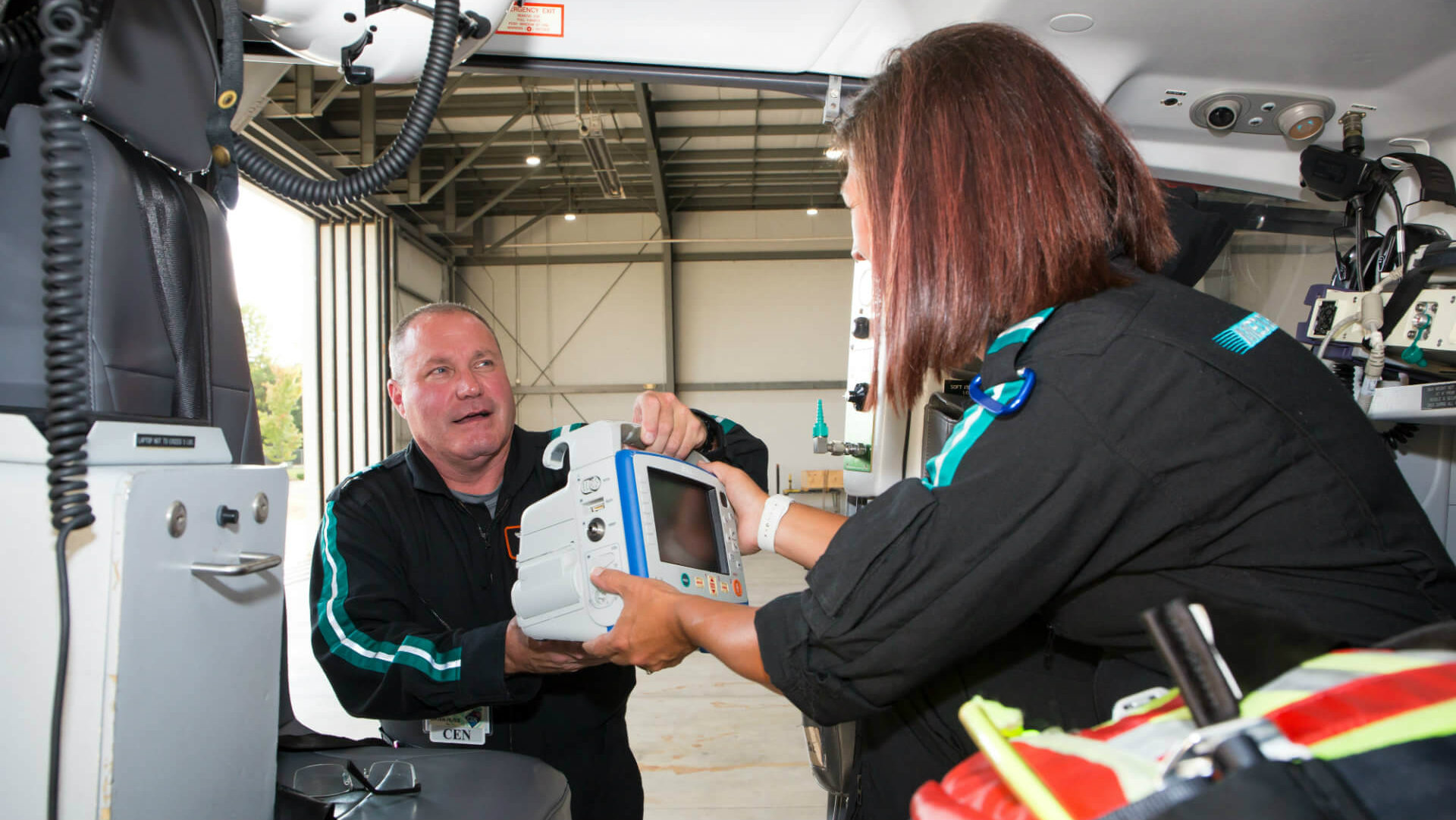 Brian Huss, RN, hands a medical monitor to Erica Cook, RN, as the members of Atrium Health's MedCenter Air team prepare a helicopter for deployment ahead of Hurricane Florence.